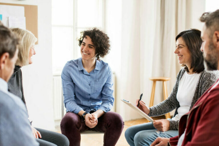Men and women sitting in a circle during group therapy, talking.