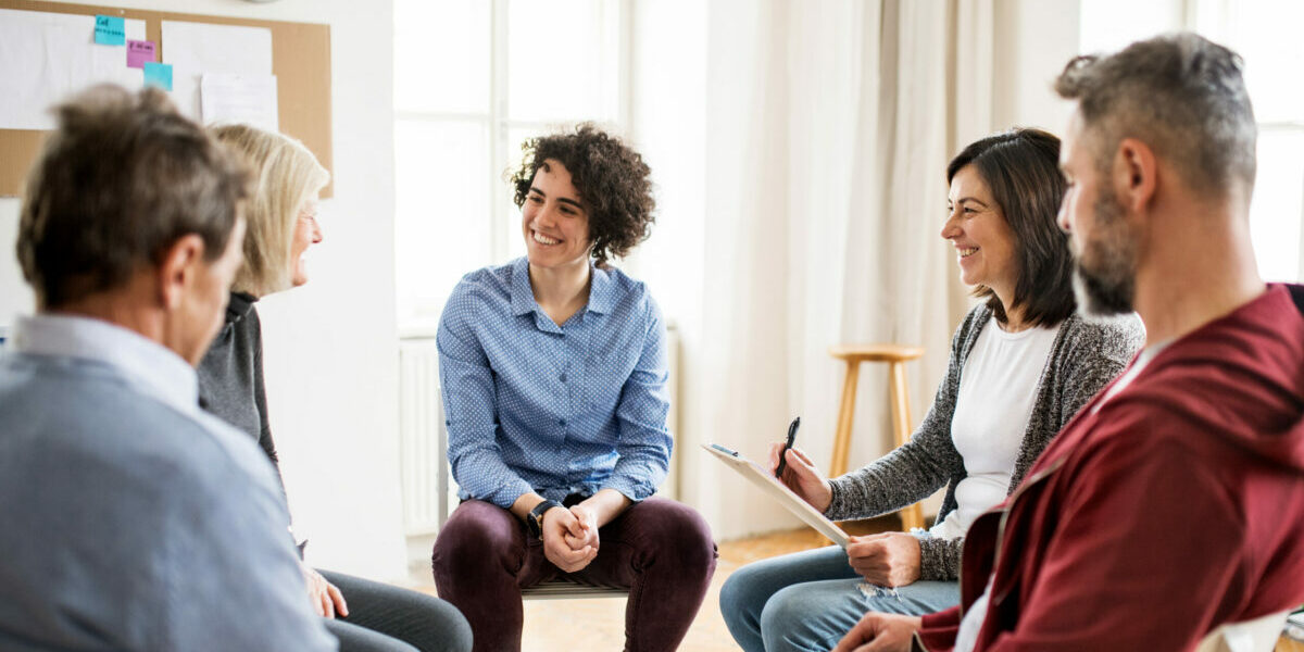 Men and women sitting in a circle during group therapy, talking.